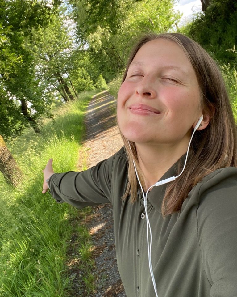 Privates Foto von Lara Katharina Aberle bei einem Spaziergang Frau mit geschlossenen Augen, die lächelt und die Arme ausbreitet, umgeben von Natur.