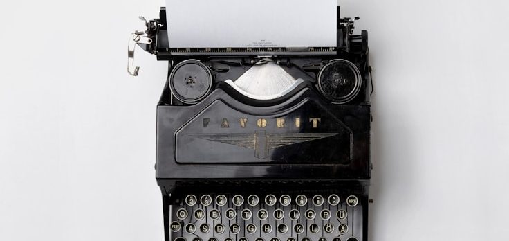 Foto von Florian Klauer von Unsplash Schwarze Schreibmaschine mit leeren Seiten und Retro-Design.